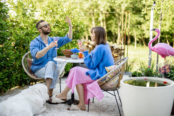 Young stylish couple have conversation while sitting by the round coffee table at their beautiful garden. Young man and woman have romantic evening outdoors