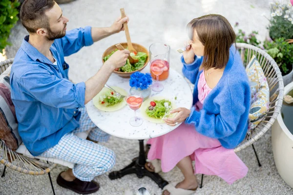 若く明るいカップルは 屋外の丸いテーブルに座っている間に健康的なサラダを食べ 夏の飲み物を飲みます 上からの眺め — ストック写真