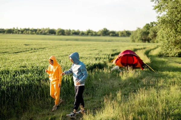 夏の間 緑のフィールドでテントと一緒に旅行しながら 若いカップルは楽しみ 話し合います — ストック写真