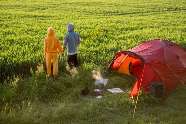 自然の中をテントで旅しながら 若いカップルは美しい夕日の景色をお楽しみください 男と女は夏の時間を一緒にキャンプ場で過ごす緑のフィールド上のテント — ストック写真