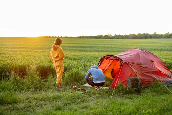 若いカップル料理 緑のフィールドのキャンプ場で一緒に夏の時間を過ごす 男と女は自然の中でテントと一緒に旅行 — ストック写真