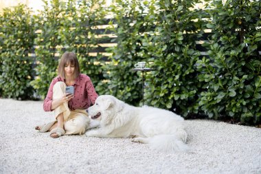 Genç bir kadın kocaman beyaz sevimli köpeğiyle rahatça oturup arka bahçede vakit geçiriyor. Evcil hayvanlarla arkadaşlık ve açık havada iyi vakit geçirme kavramı.