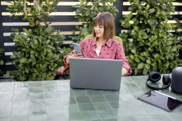 Young woman works on laptop and phone at outdoor workspace in the garden. Concept of remote work from comfortable home office or work during vacations