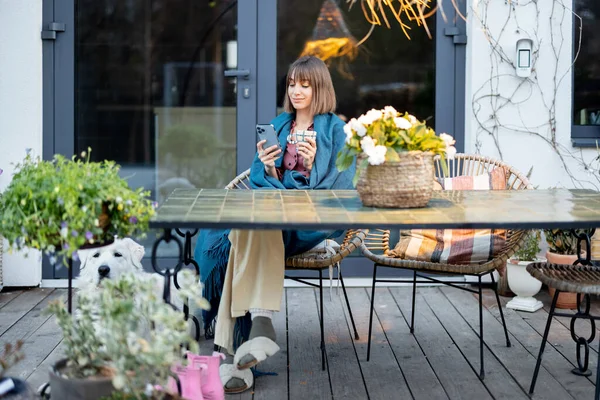 身着格子花裙的年轻女子 晚上坐在餐桌旁 享受着在温馨的家平台上与花朵共饮的乐趣 — 图库照片