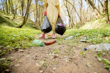 Koruyucu elbiseli bir kadın çöp torbalarıyla ormanda plastik topluyor. Kesilmiş manzara. Yatak ekolojisi ve çevre kirliliği sorunu uzun zamandır çürümekte olan atıkla
