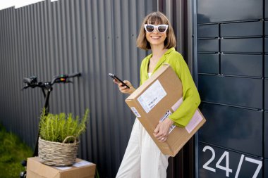 Otomatik posta terminalinin yanında duran ve elektrikli scooterla mal getiren genç bir kadının portresi. Modern teknolojiler ve sürdürülebilir yaşam tarzı kavramı