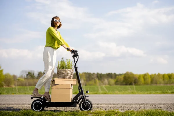 Young Woman Driving Electric Scooter Parcels Flowerpot Field Road Summer — Zdjęcie stockowe