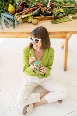 Kadın taze gıda malzemeleriyle dolu masanın yanında otururken biraz limonata içiyor. Sağlıklı beslenme ve yaşam tarzı kavramı