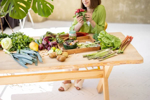 Young Woman Sits Table Full Fresh Food Ingredients Room Green — Φωτογραφία Αρχείου