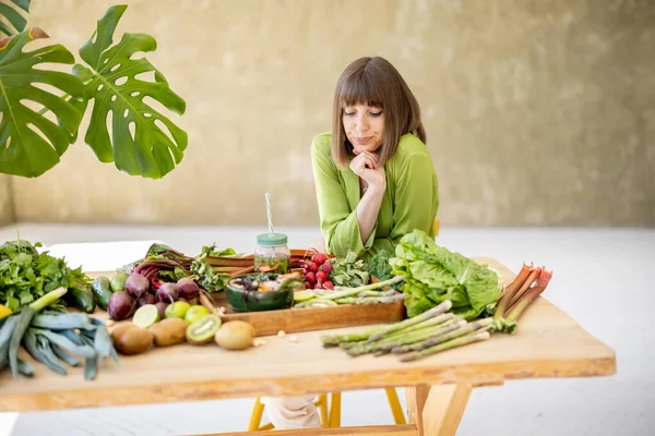 Young Woman Sits Table Full Fresh Food Ingredients Room Green — Stok fotoğraf