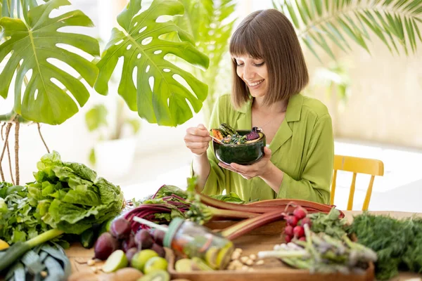 年轻而快乐的女人一边坐在餐桌旁一边吃素食碗 一边吃着新鲜蔬菜 水果和蔬菜 健康的天然饮食和生活方式概念 — 图库照片