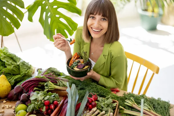 一个年轻而快乐的女人坐在餐桌旁 满满的新鲜蔬菜 水果和蔬菜 她的画像就是她吃素食碗 健康的天然饮食和生活方式概念 — 图库照片