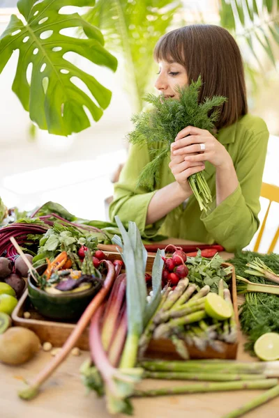 一个年轻而快乐的女人的画像 当她坐在满是新鲜蔬菜和水果的桌旁时 手里拿着一堆绿叶 健康饮食和生活方式概念 — 图库照片