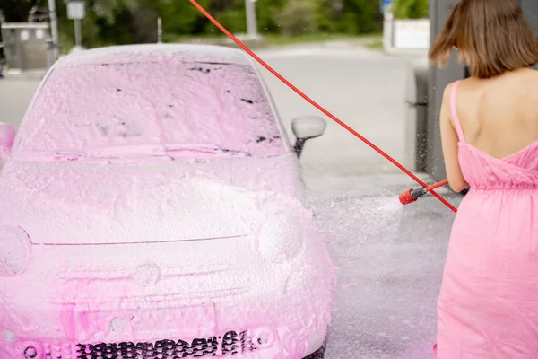 Person washing tiny car with nano foam at car wash during summer time. Close-up view on car in foam and washing gun