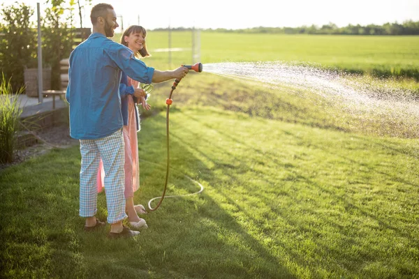日落时 一对可爱的夫妇在他们乡间房子的后院浇灌草坪 照顾花园的年轻家庭在一起度过夏天 — 图库照片