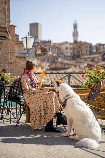 Woman feeds her dog while sitting at restaurant with beautiful view on Siena town. Traveling Tuscany region in Italy. Concept of italian cuisine