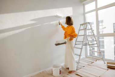 Woman paints the wall in white color while making repairment in newly purchased apartment. Repair and house renovation concept