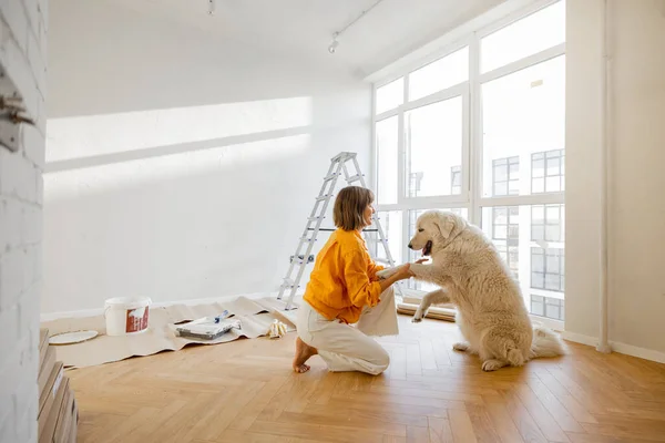 Young woman plays with her dog in room while making repairing in apartment. Fun during house renovation and friendship with pets concept