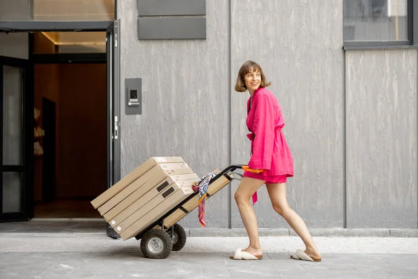 Woman carries furniture in boxes on a cart, delivering them home. Process of self improvement apartment, buying furniture and delivery