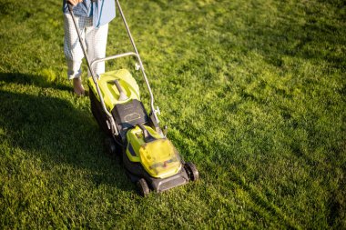 Man mows the lawn with lawn mower, close-up on machine. Concept of modern electric wireless garden equipment
