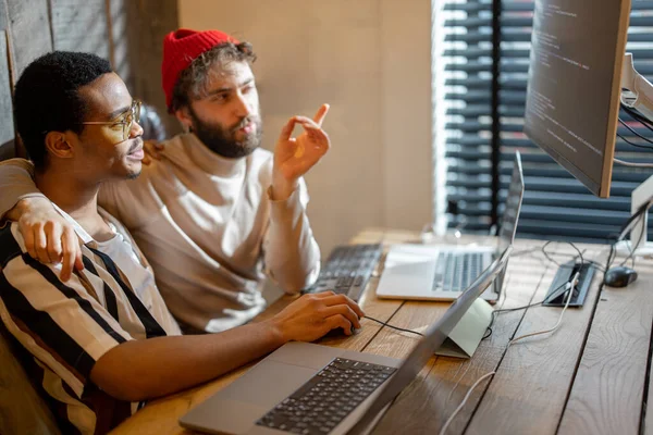 Two men with different nationality programming on computers, sitting at cozy home office. Concept of freelance and remote work. Iea of gay couples working together