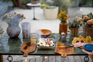 Cooking food on disposable grill on table decorated with flowers at backyard