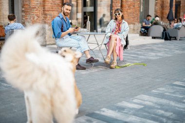 Modern ofis bölgesinde köpekler oynarken şık bir çift kafede oturuyor. Evcil hayvan konseptiyle boş zaman