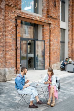 Modern ofis bölgesindeki kafe terasında otururken şık iki meslektaş sohbet ediyor. Çiftler birlikte vakit geçirip açık havada su içiyorlar.
