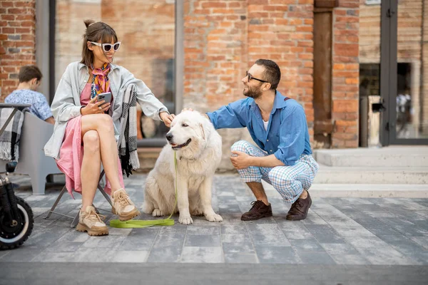 Stylish man and woman care adorable white dog while hanging out together at cafe terrace. Man flirting with woman caaring her dog