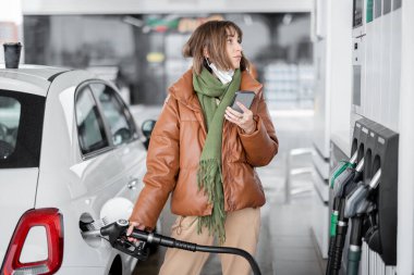 Kadın arabaya benzin dolduruyor, ödemede akıllı telefon kullanıyor. Dükkanı ziyaret etmeden hızlı yakıt ikmali için mobil teknoloji kavramı
