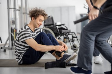 Guy wears cuffs on his legs in preparation for exercise, nurse comes to help. Concept of physical therapy for people with disabilities