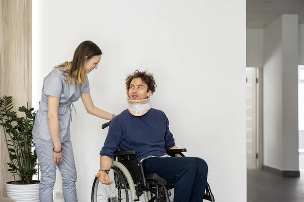 Medical worker communicates with a man in a wheelchair having neck injury. Concept of treatment and rehabilitation after injuries