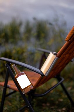 Piknikte ya da balık tutarken katlanan sandalyeye sert alkol ve matara. Yapıştırmak için boş etiketli bir şişe. Marka içeceği için maket resmi