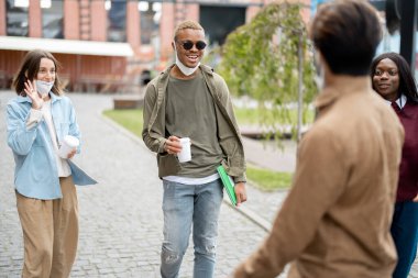 Üniversite kampüsünün sınırlarında dolaşan çok ırklı öğrenciler. Eğitim ve öğrenim kavramı. Öğrenci yaşam tarzı fikri. Tıbbi maskeli genç erkekler ve kız. Salgın sırasında sağlık koruması