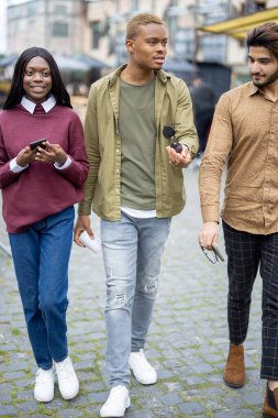 Multiracial students walking outdoors. Handsome smiling men and woman. Concept of spending time together. Blurred background of city
