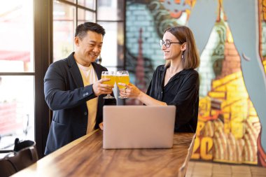 Modern bir barda konuşan ve bira içen çok ırklı arkadaşlar ya da iş ortakları. Dinlenme ve rahatlama kavramı. Barda içerken iş anlaşması. Memnun genç Avrupalı kadın ve yetişkin Asyalı adam