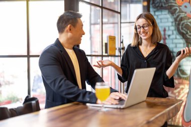 Modern bir barda konuşan ve bira içen çok ırklı arkadaşlar ya da iş ortakları. Dinlenme ve rahatlama kavramı. Barda içerken iş anlaşması. Memnun genç Avrupalı kadın ve yetişkin Asyalı adam