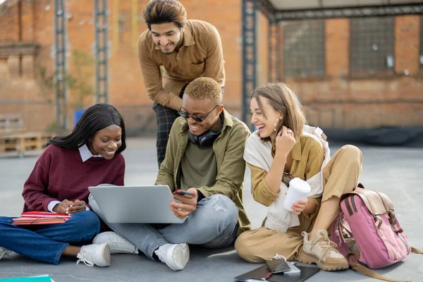 Multiracial students sit and learn on asphalt at university campus. Concept of education. Remote and e-learning. Idea of student lifestyle. Girls and black guy using laptop. Indian guy reading book