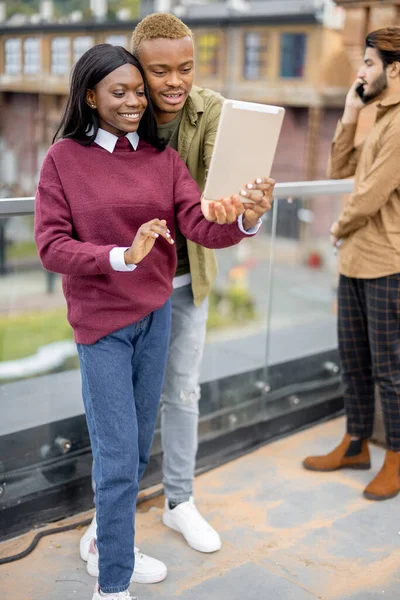 Black students having video call on digital tablet outdoors. Concept of remote and e-learning. Idea of students lifestyle. Smiling young girl and guy. Man waving hand. University campus