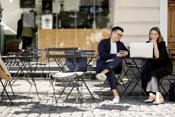 Multiracial business people watching something on laptop during work at outdoor cafe. Concept of remote and freelance work. Idea of teamwork and business cooperation. Caucasian woman with smartphone