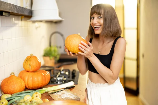 Portrait of a cheerful woman holds pumpkin vegetables while cooking healthy food in kitchen. Concept of vegetarian food and autumn pumpkin menu