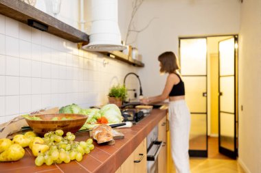 Young woman washes ingredients while cooking healthy vegetarian food in kitchen at modern and stylish apartment. Healthy lifestyle and eating concept