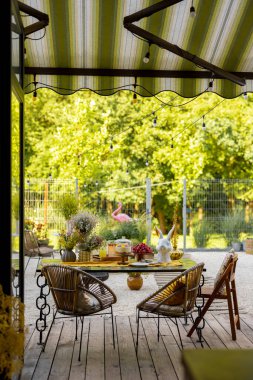 Beautiful and cozy dining place on wooden terrace at backyard. Cheese cake on garden table decorated with flowers