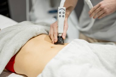 Applying vacuum roller massage for womans abdomen using a special nozzle at beauty medical center, close-up. Concept of modern medical procedures for beauty