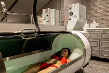 Woman lying in oxygen capsule, having deep rest and recovery during the medical procedure of filling the body with oxygen
