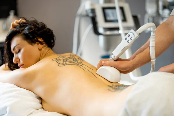 Woman receiving vacuum roller massage on her back at medical beauty centre. Lymphatic drainage massage procedure. Womans back with tattoos