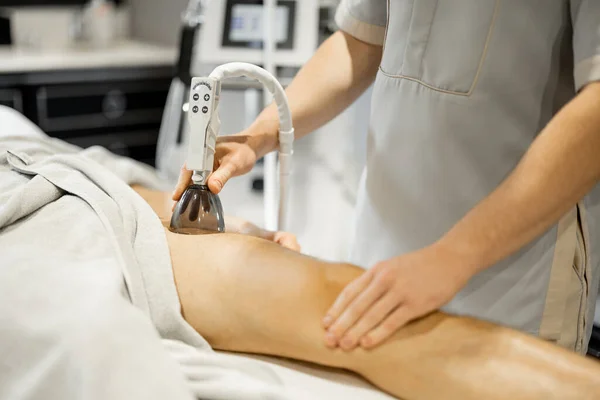 Applying vacuum roller massage on male leg using a special nozzle at beauty medical center, close-up. Concept of modern medical procedures for beauty