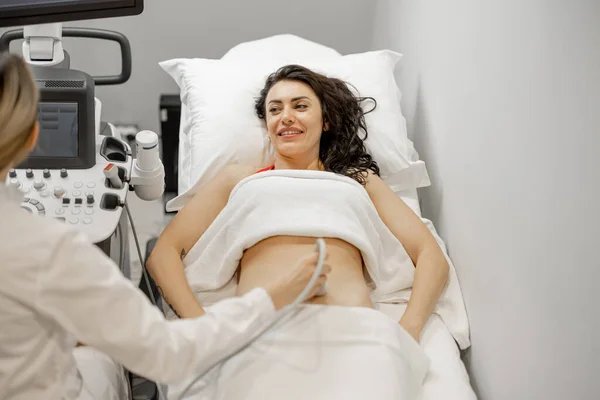 Happy adult woman during an ultrasound examination of the abdominal cavity at modern medical office. Concept of womens health and examination during pregnancy