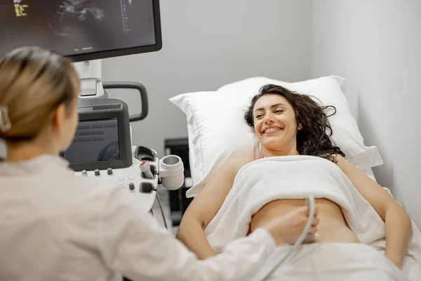 Happy adult woman during an ultrasound examination of the abdominal cavity at modern medical office. Concept of womens health and examination during pregnancy