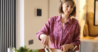 Evde mutfakta sağlıklı yemek pişirirken salata yapan genç bir kadın. Sağlıklı yaşam tarzı ve sağIık kavramı